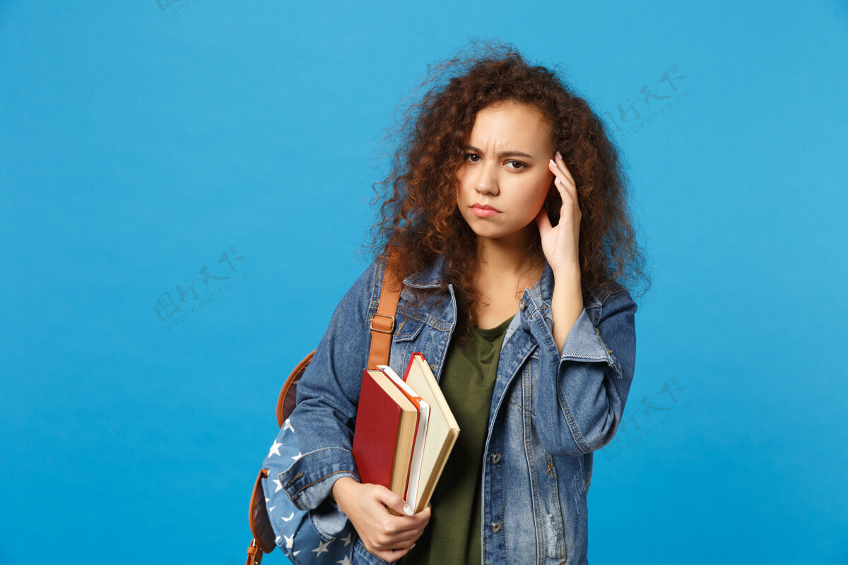 班级穿着牛仔服 背着书包的悲伤的年轻学生把书孤立地放在蓝色的墙上延迟打扰哭泣