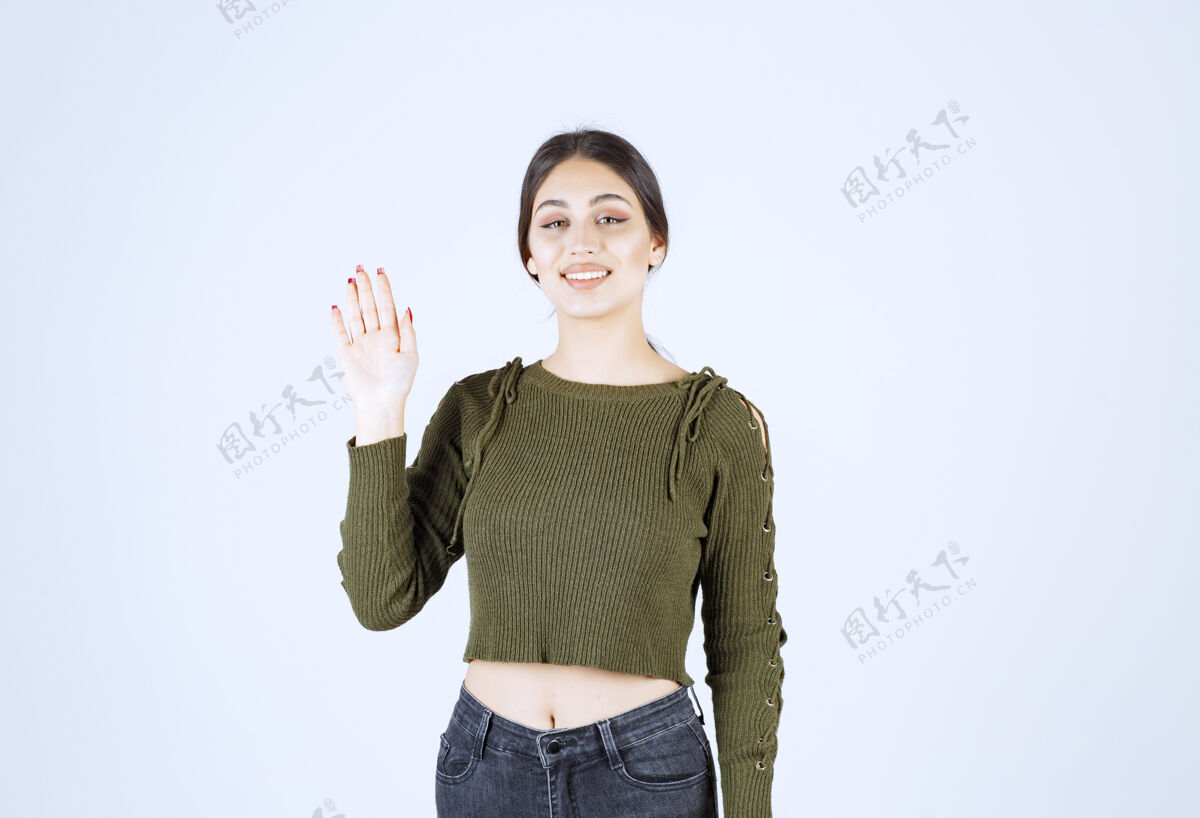 女人一个穿着绿色毛衣微笑的年轻女子挥舞着一只手挥手摆姿势微笑