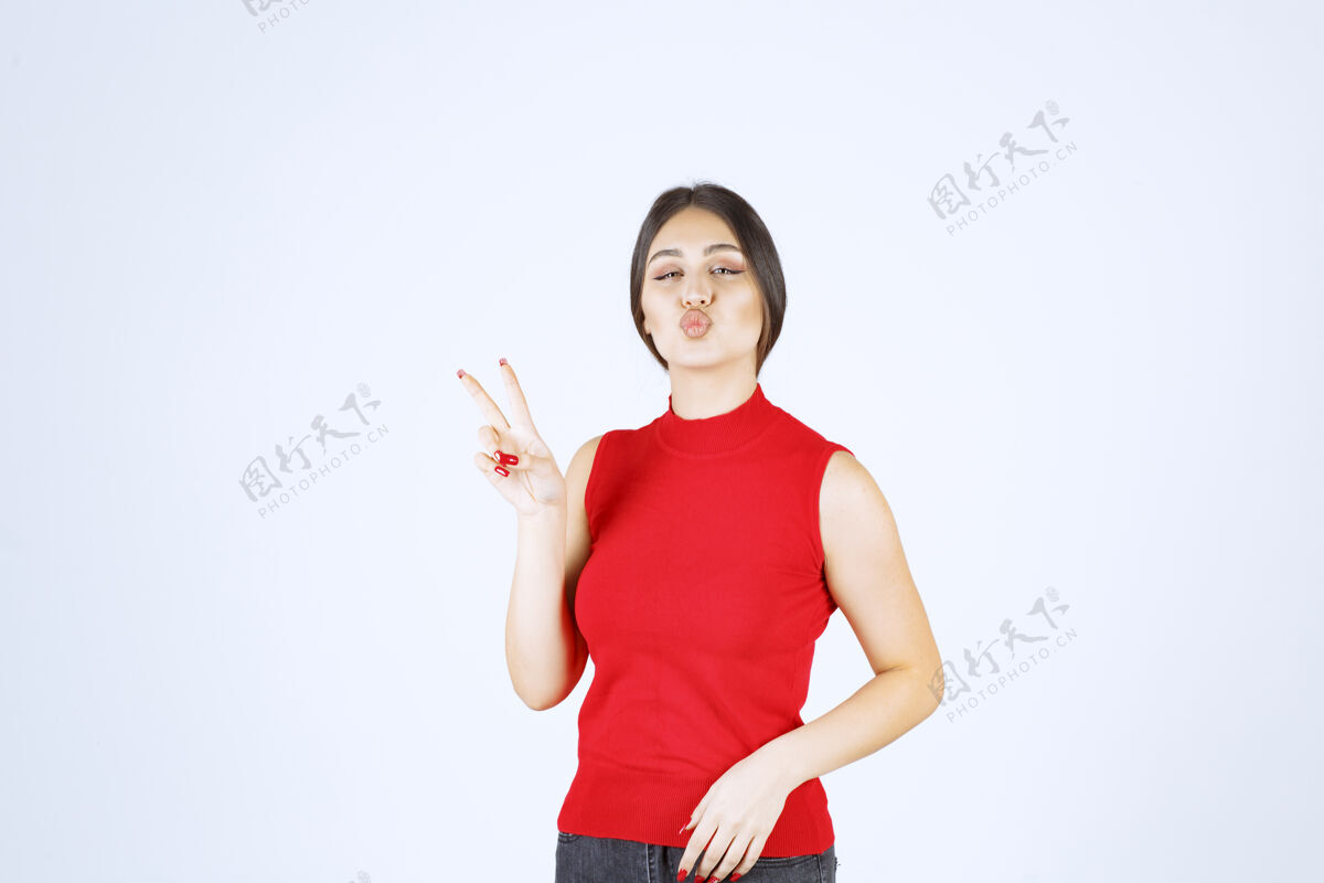 年轻穿红衬衫的女孩展示和平和友谊的标志人模特姿势