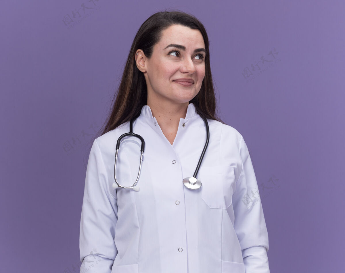 紫色高兴的年轻女医生穿着医用长袍用听诊器看着身边医生年轻女