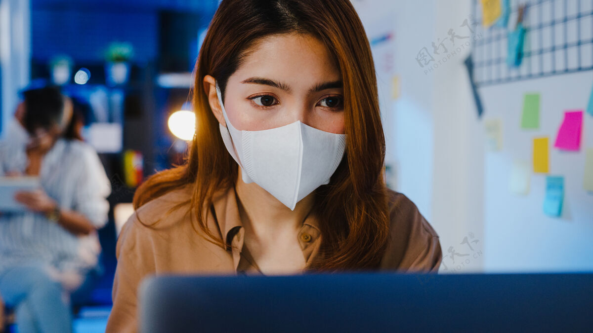 自由职业者快乐的亚洲女商人戴着医用口罩 在新的正常情况下保持社交距离 以防病毒 晚上在办公室使用笔记本电脑过度工作社交工作区