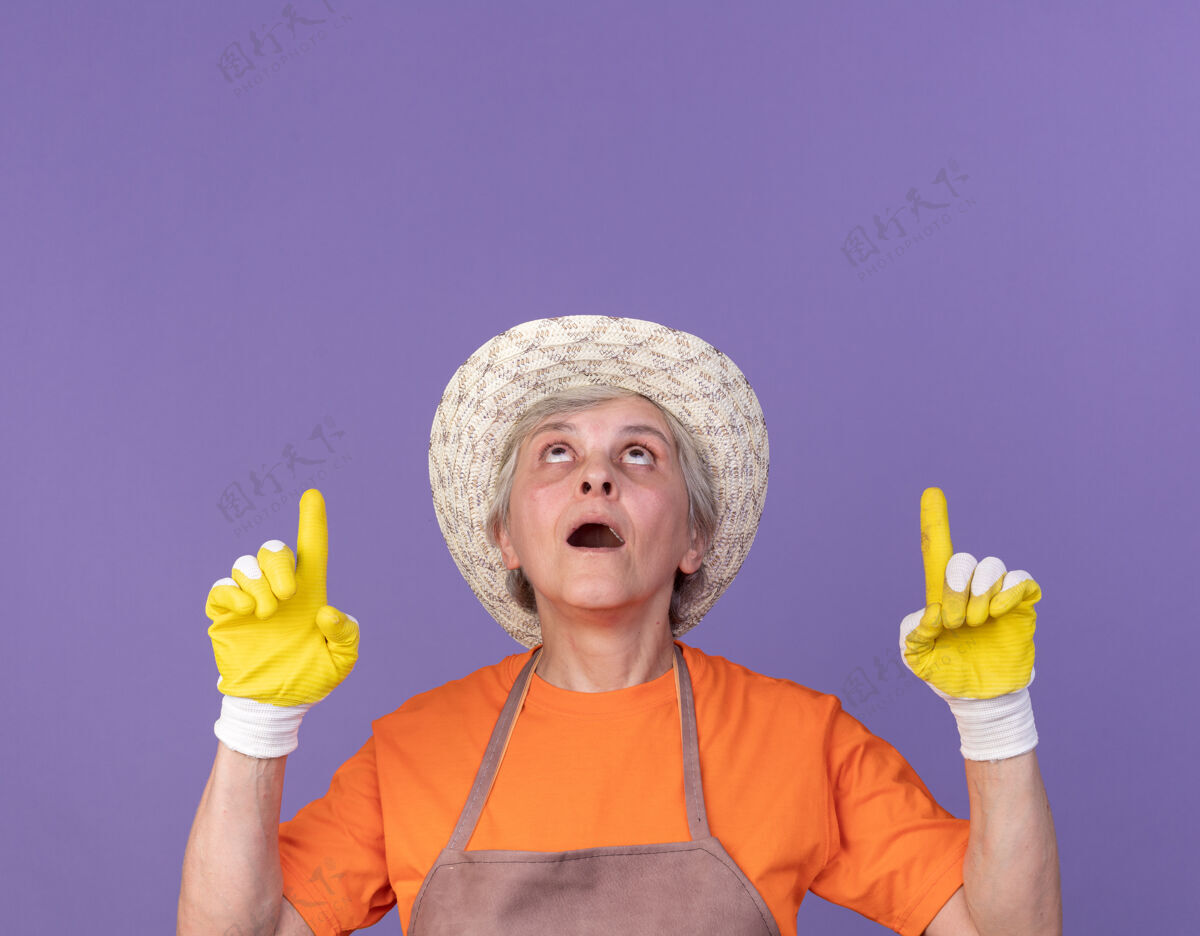手套兴奋的上了年纪的女园丁戴着园艺帽和手套看着并指着头园艺向上女