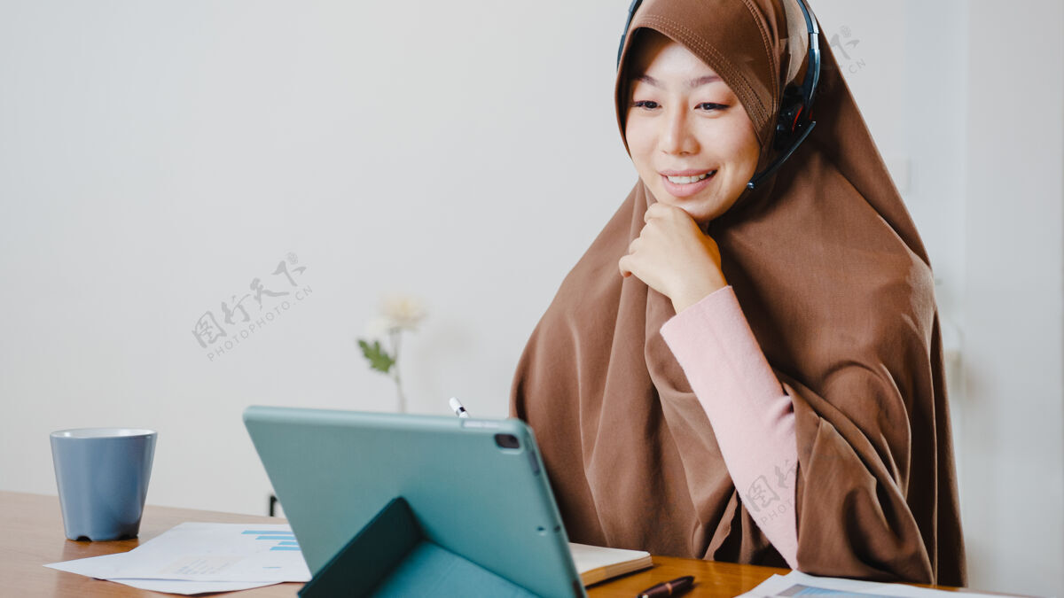 商务女性穆斯林女士戴着耳机使用数字平板电脑在家里厨房工作时 通过视频会议与同事谈论销售报告耳机远程伊斯兰
