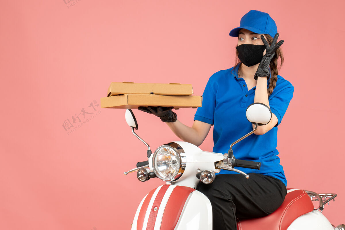 面具俯视图集中女快递员戴着医用面罩和手套坐在滑板车上传递粉彩桃背景的命令手套焦点医疗