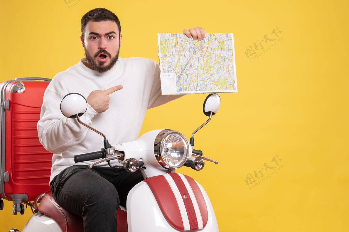 地图顶视图好奇的年轻人坐在摩托车上 手提箱上拿着地图 背景是孤立的黄色年轻人车辆摩托车