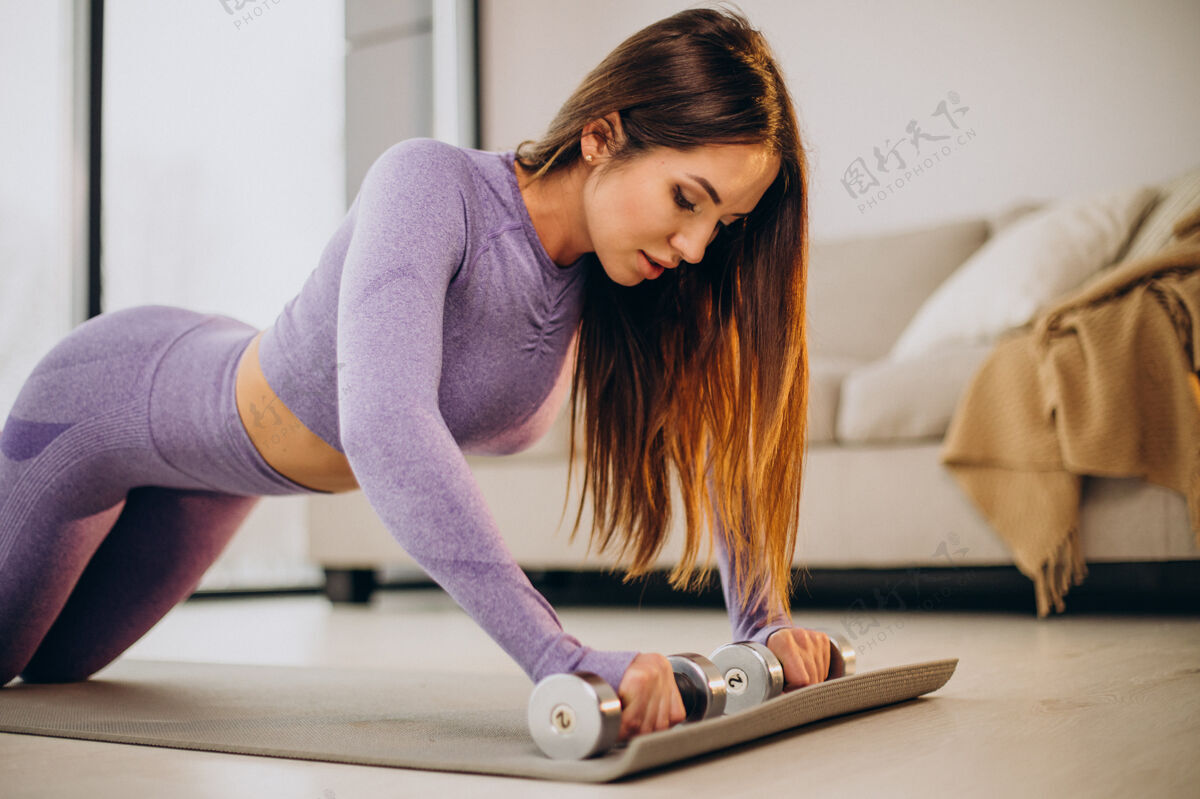 形状年轻女子在家里的垫子上练习哑铃运动运动装体重