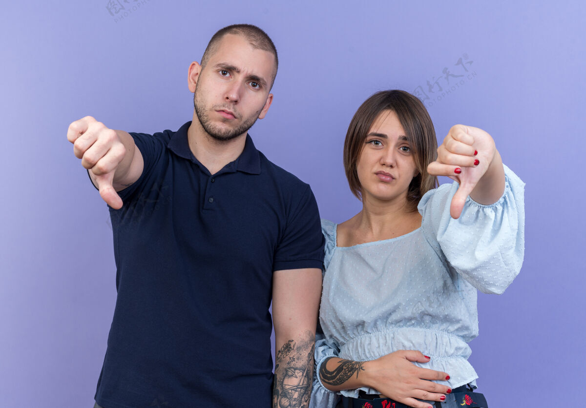 向下年轻漂亮的夫妇不高兴地竖起大拇指站在蓝色的墙上站女人人