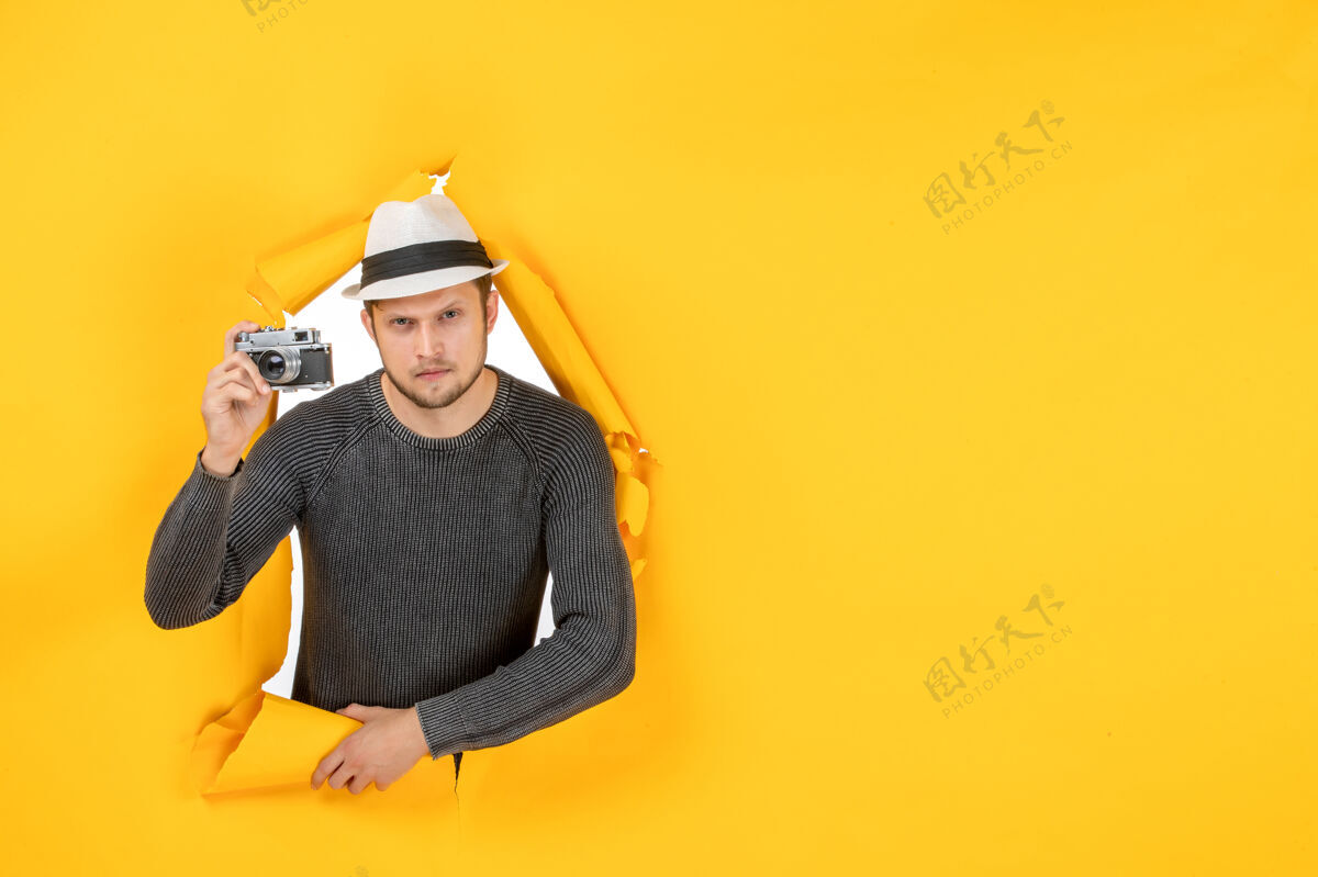 牛仔帽在一个撕破的黄色墙壁上 一个拿着相机帽子的人的正视图微笑破烂工作