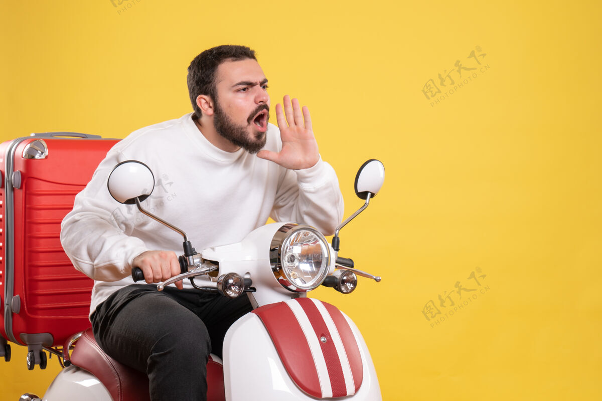 男性俯视图：一个年轻人坐在摩托车上 背着手提箱 在孤立的黄色背景下 用惊讶的表情呼唤着某人面部摩托车年轻人