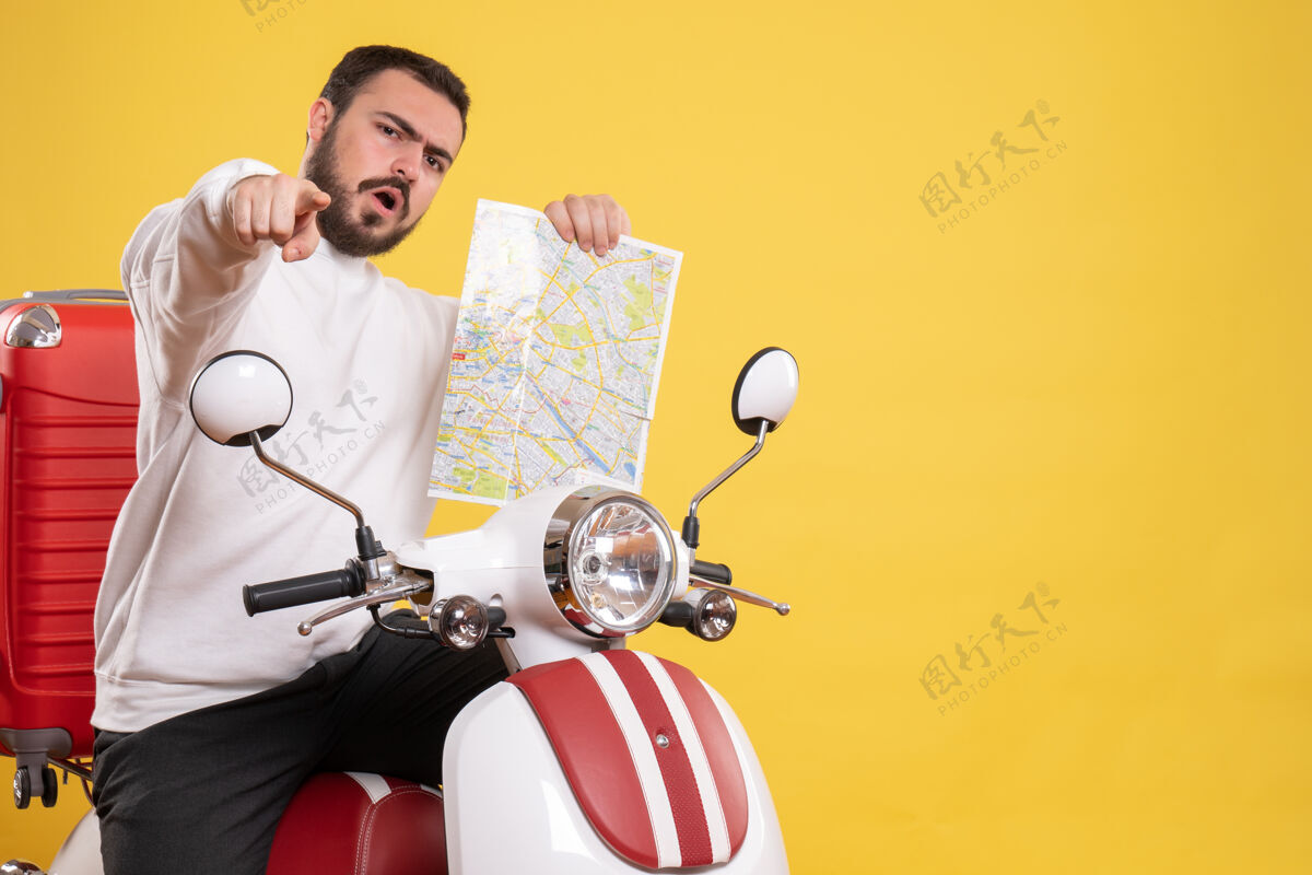 向前顶视图好奇的家伙坐在摩托车上 手提箱上拿着地图 在孤立的黄色背景上指向前方摩托车地图背景
