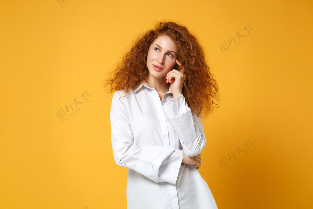 白种人沉思的年轻红发女女孩穿着休闲白衬衫在黄橙色的墙上摆出孤立的姿势橙色梦想女孩