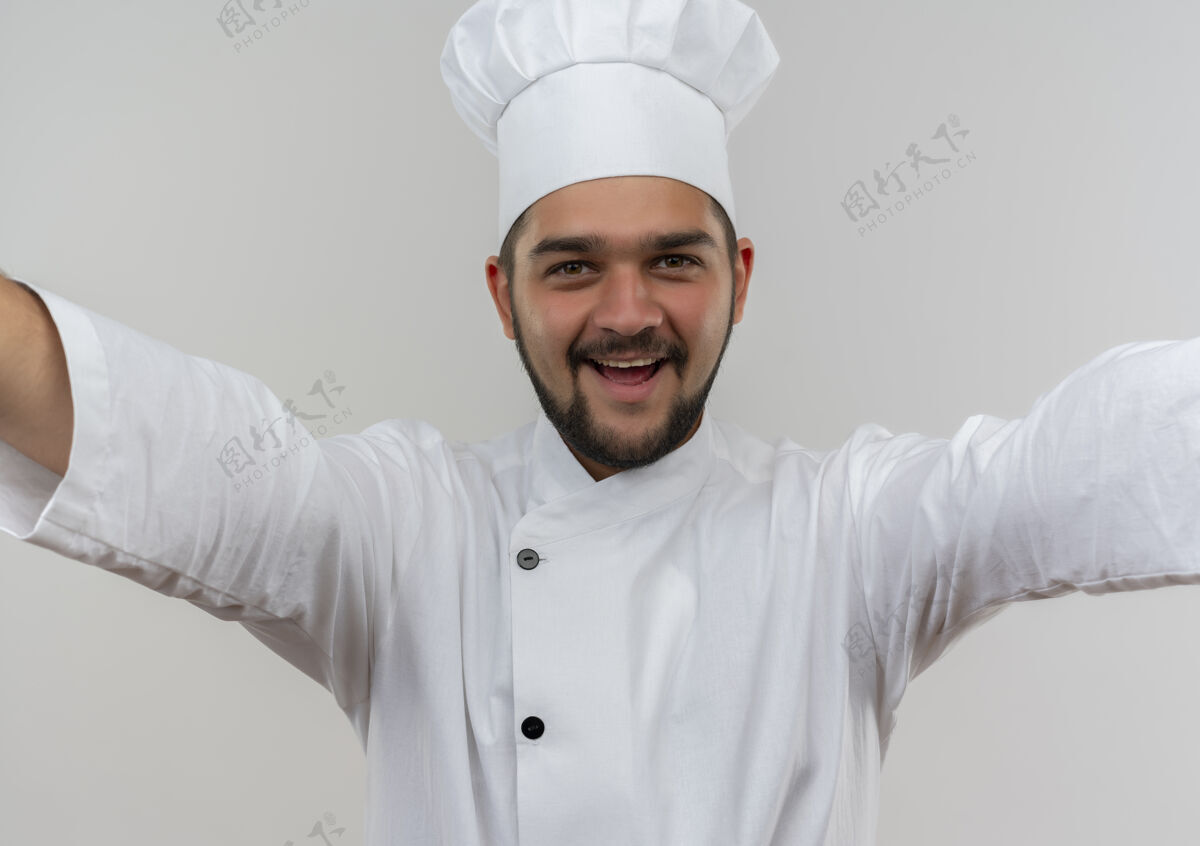 制服身着厨师制服的快乐年轻男厨师张开双臂 孤零零地站在白墙上厨师开放男性