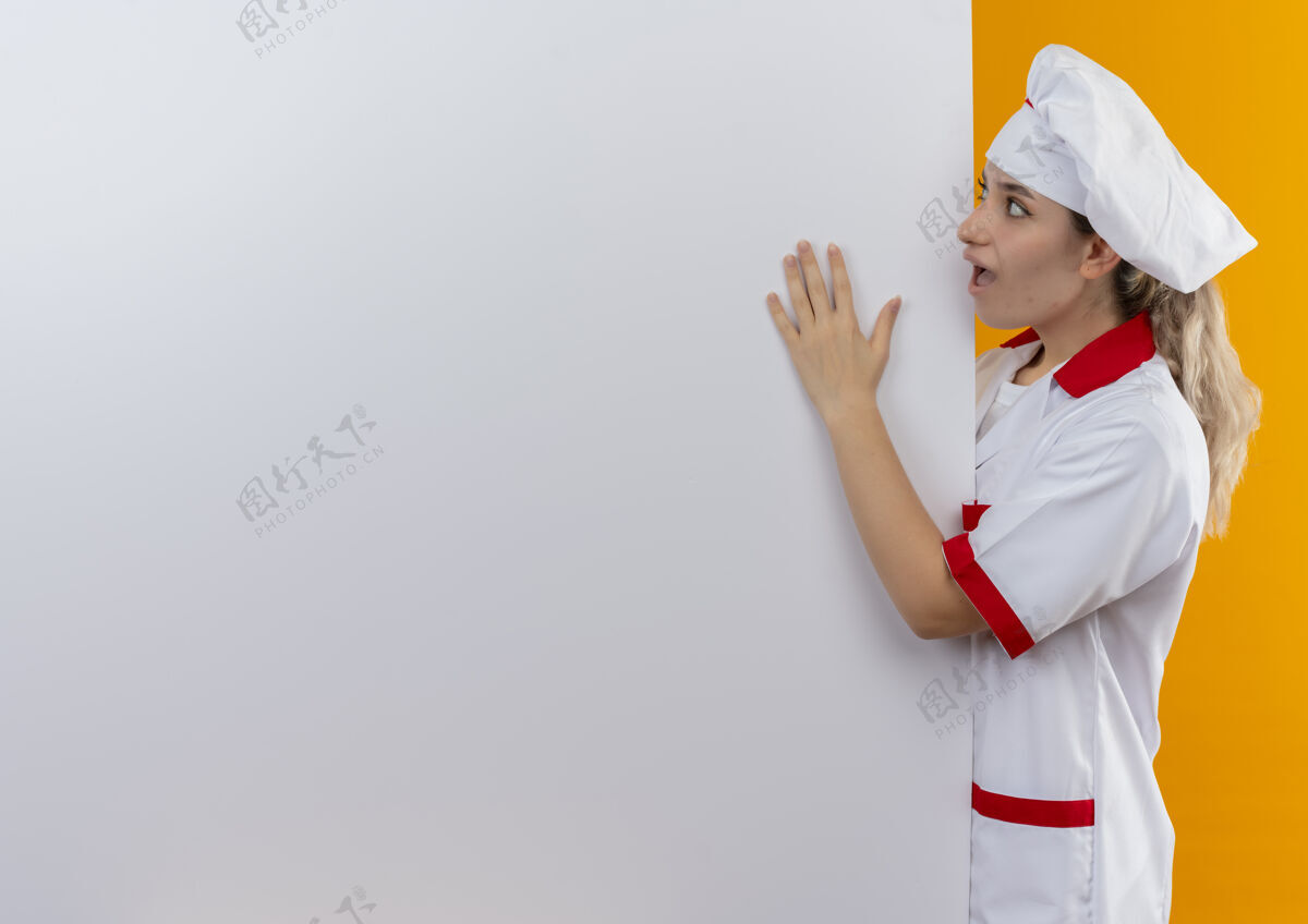 厨师年轻漂亮的厨师穿着厨师制服站在后面看着 把手放在白色的墙上 橙色的墙上隔离着复制空间手漂亮印象