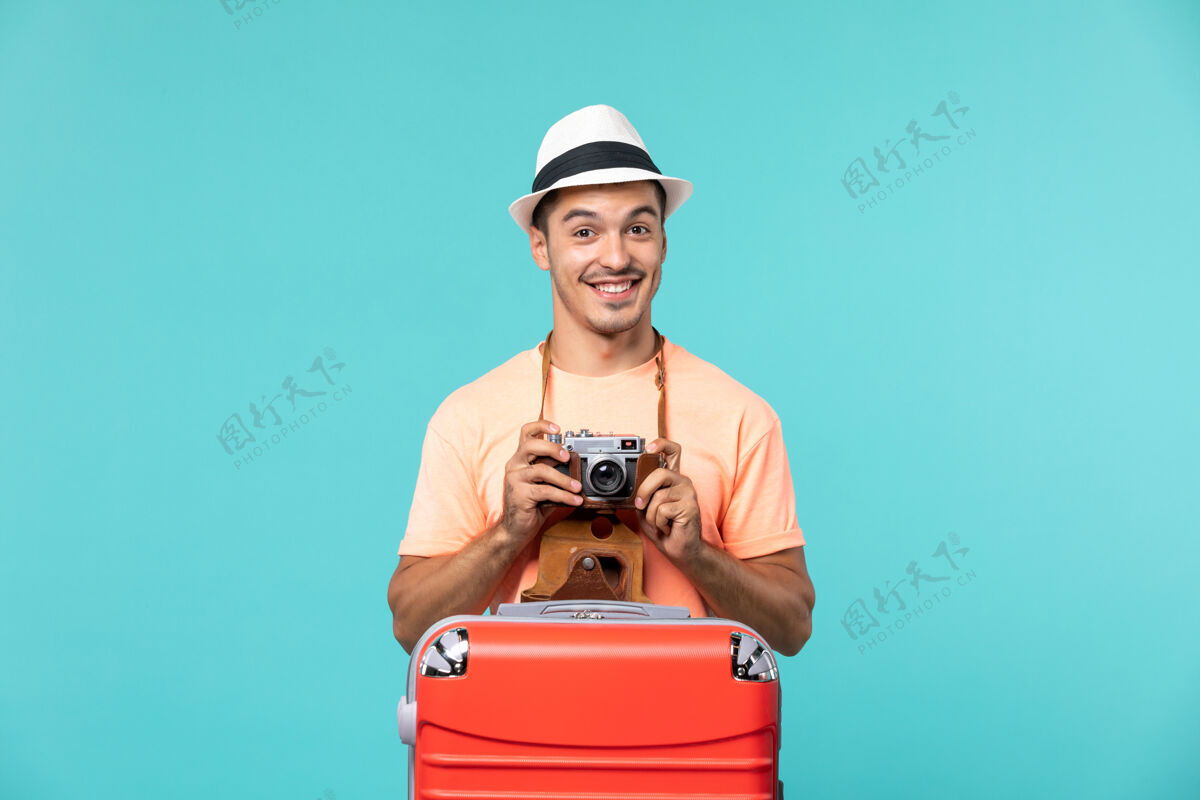 旅行带着红色手提箱的度假男人用蓝色的相机拍照帽子旅行人