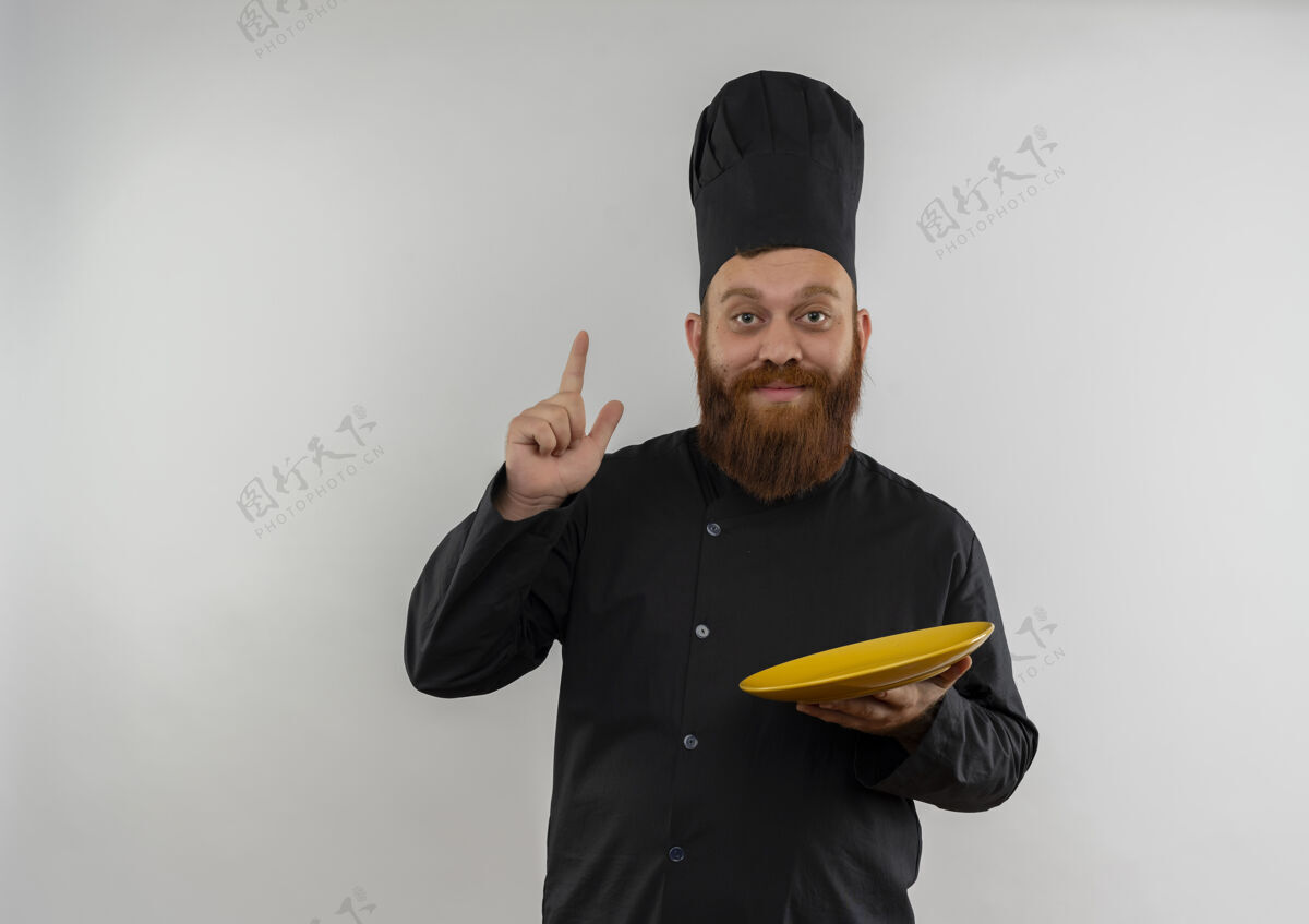 空印象深刻的年轻帅哥厨师在厨师制服举行空盘子和提高手指隔离在白色墙壁上复制空间制服印象年轻