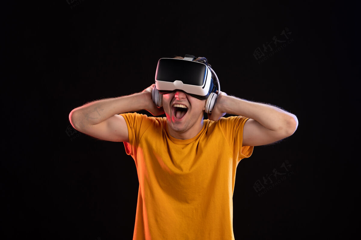 视觉在黑暗的墙上 年轻人戴着耳机玩虚拟现实的画像成人男人男性