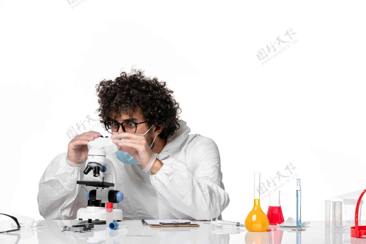 防护男医生穿着防护服 戴着口罩 用显微镜对着白色实验室面罩办公室