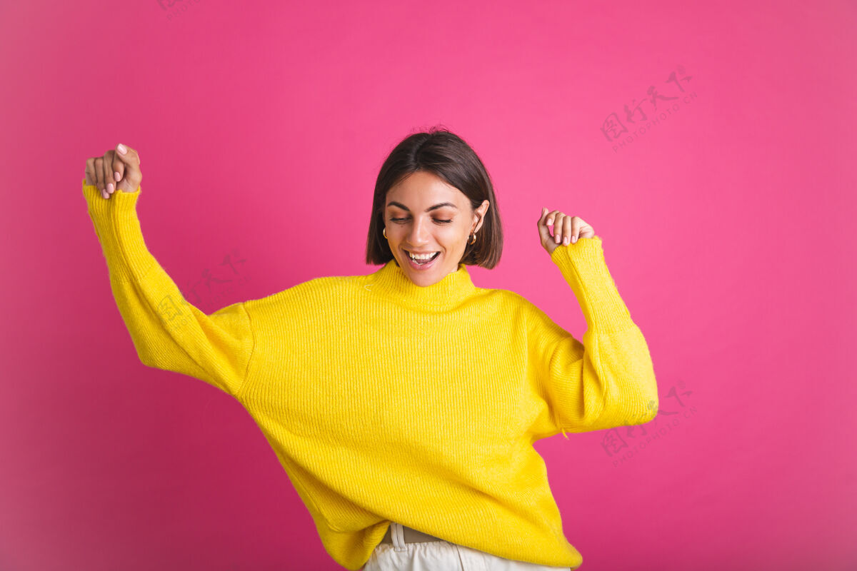 表情美丽的女人穿着鲜艳的黄色毛衣孤立在粉红色快乐兴奋的舞蹈动人的微笑积极明亮寒冷