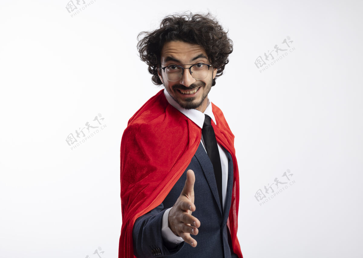 持有年轻的高加索超级英雄微笑着 戴着眼镜 穿着红色斗篷的西装 伸出手来光学微笑年轻
