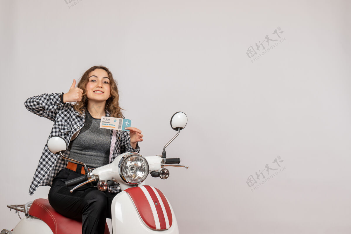 摩托车坐在轻便摩托车上的年轻女孩拿着车票竖起大拇指坐成人人