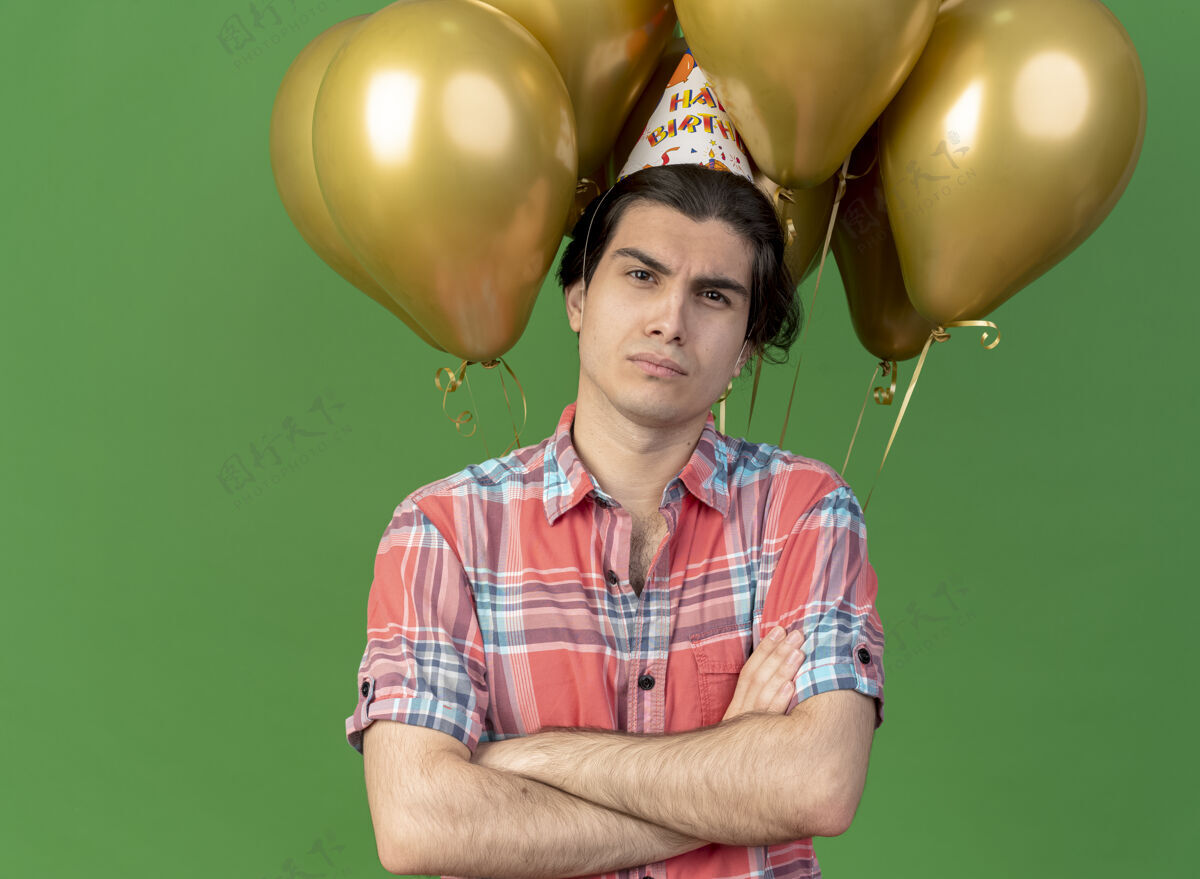 男士自信英俊的白种人戴着生日帽交叉双臂站在氦气球前看着相机正面自信绿色