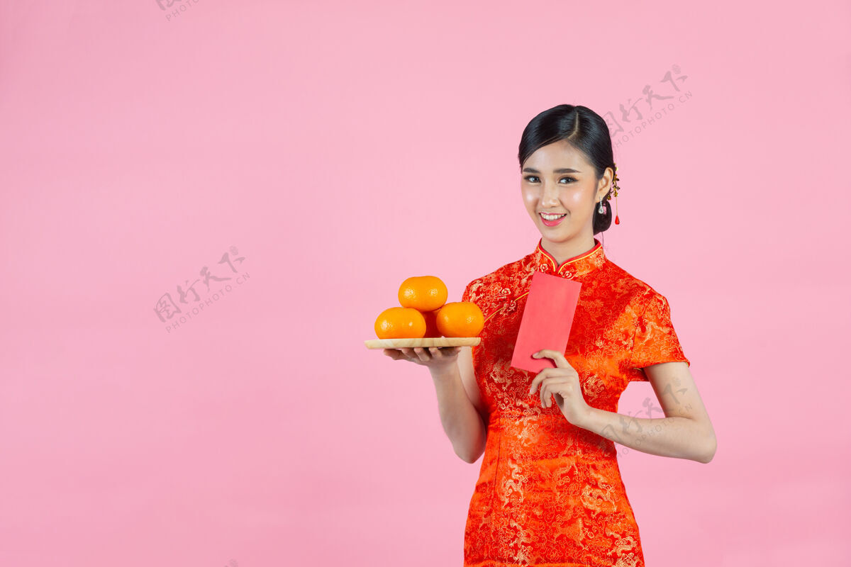 东方美丽的亚洲女人开心地微笑着 手里拿着粉红背景的新鲜橘子过年年轻展示欢呼