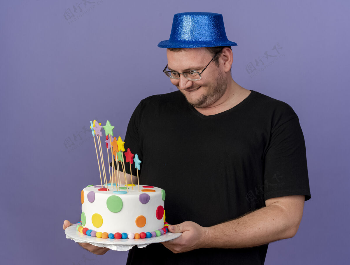 空间兴奋的成年斯拉夫人戴着眼镜 戴着蓝色派对帽 拿着生日蛋糕看着复制聚会紫色