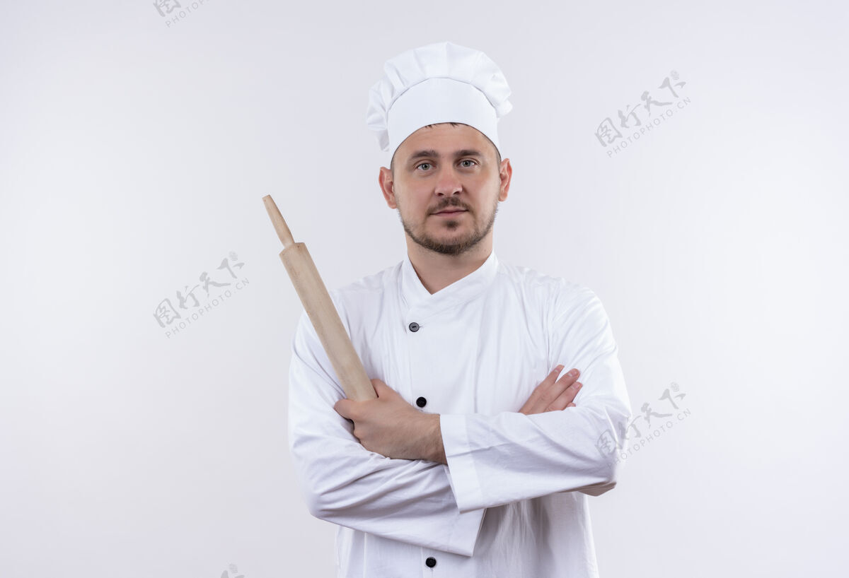 制服自信的年轻帅哥厨师身着厨师制服 站着封闭的姿势 拿着擀面杖孤立地站在白墙上厨师姿势封闭