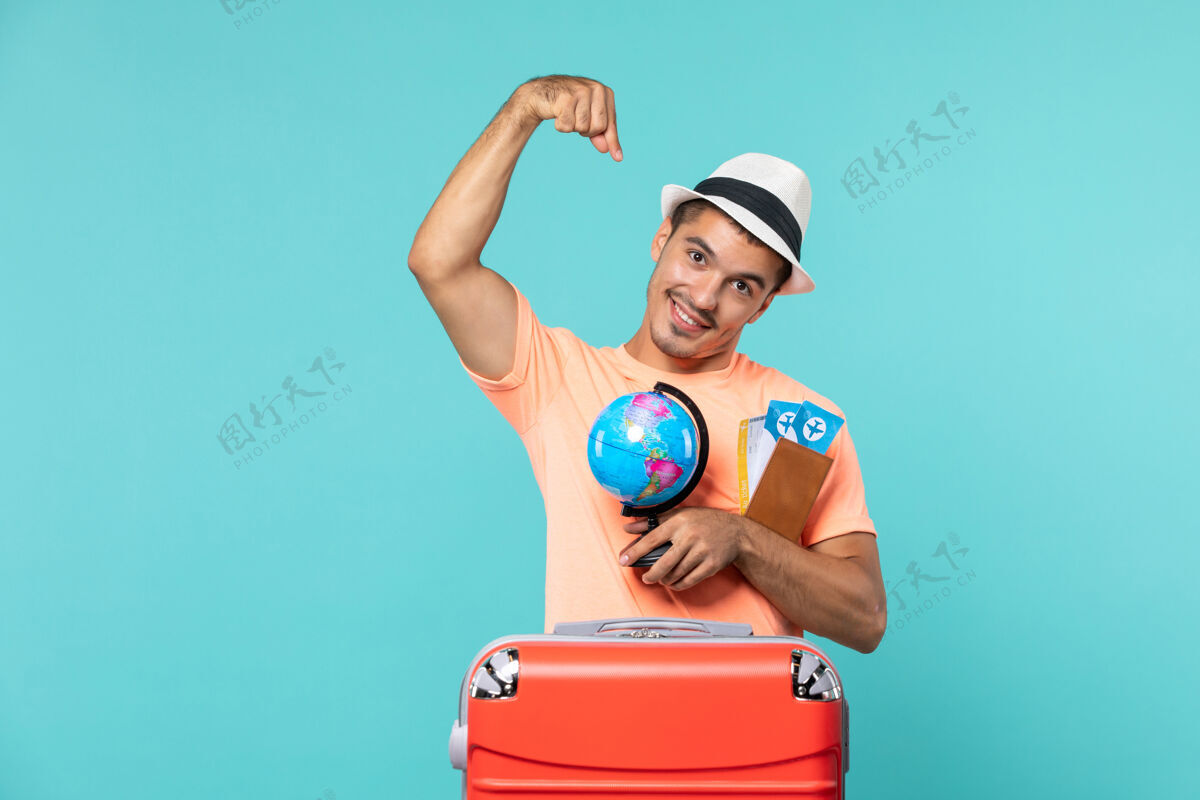 举行度假的男人拿着小地球仪和浅蓝色的机票锻炼旅程地球仪