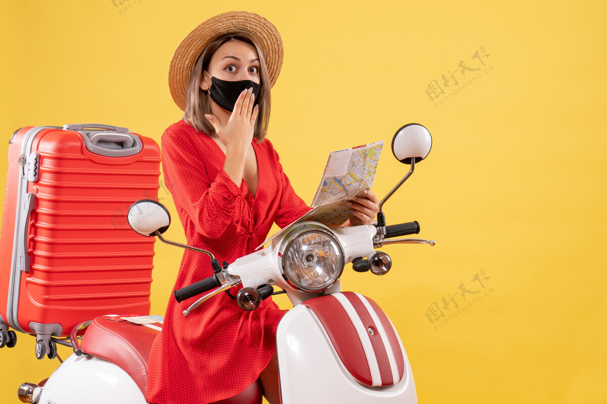 面具一位戴着黑色面具的年轻女士拿着地图 惊讶地靠近轻便摩托车惊讶的小姐摩托车黑色