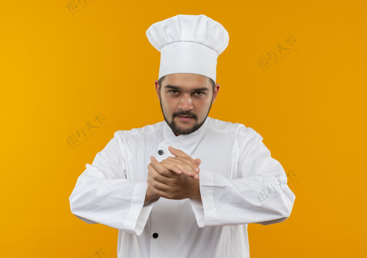 手自信的年轻男性厨师身着厨师制服 手在橙色的墙上保持着隔离男性制服烹饪