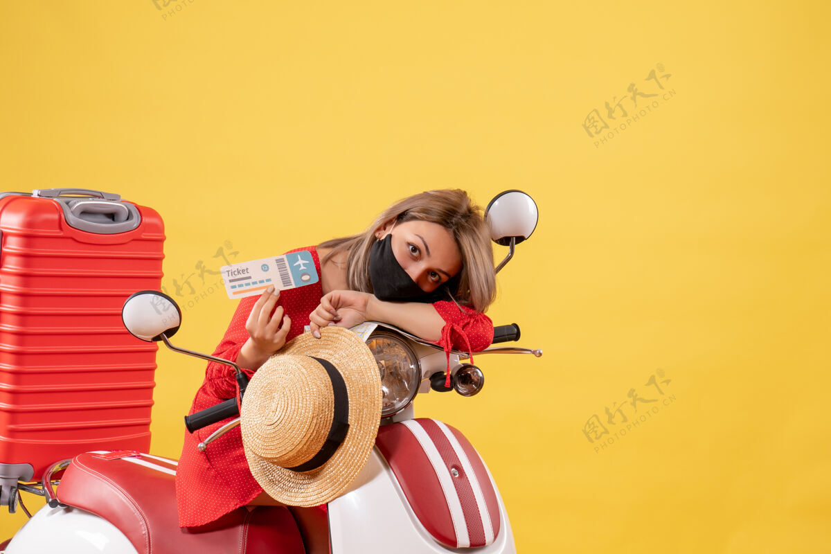 面具坐在轻便摩托车上的疲惫的年轻女士 手里拿着红色的手提箱 手里拿着车票红色手提箱肖像