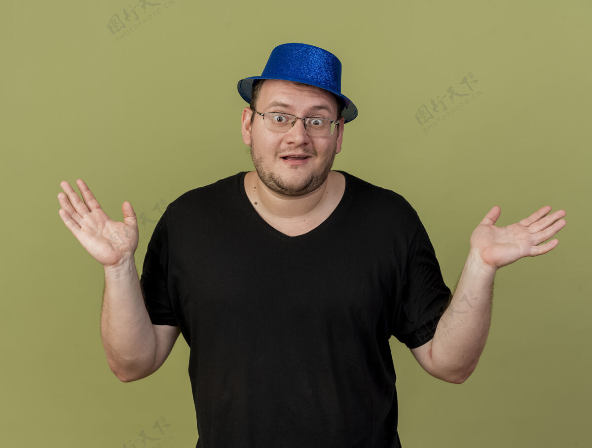 绿色令人印象深刻的成年斯拉夫人戴着眼镜 戴着蓝色派对帽 举手站立复制斯拉夫蓝色