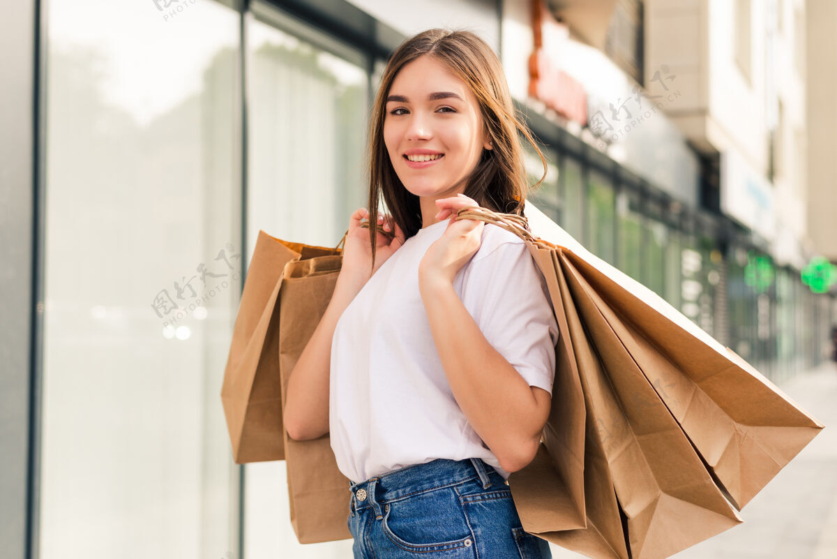 围棋带着购物袋走在街上的年轻快乐的女人持有折扣漂亮