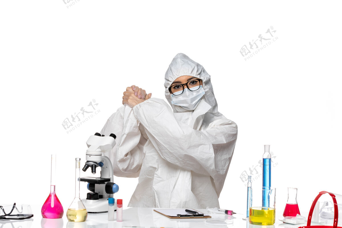 外套正面图年轻的女化学家穿着特殊的防护服 坐在桌子前 用浅白背景病毒的解决方案实验室的covid健康化学桌子人医生