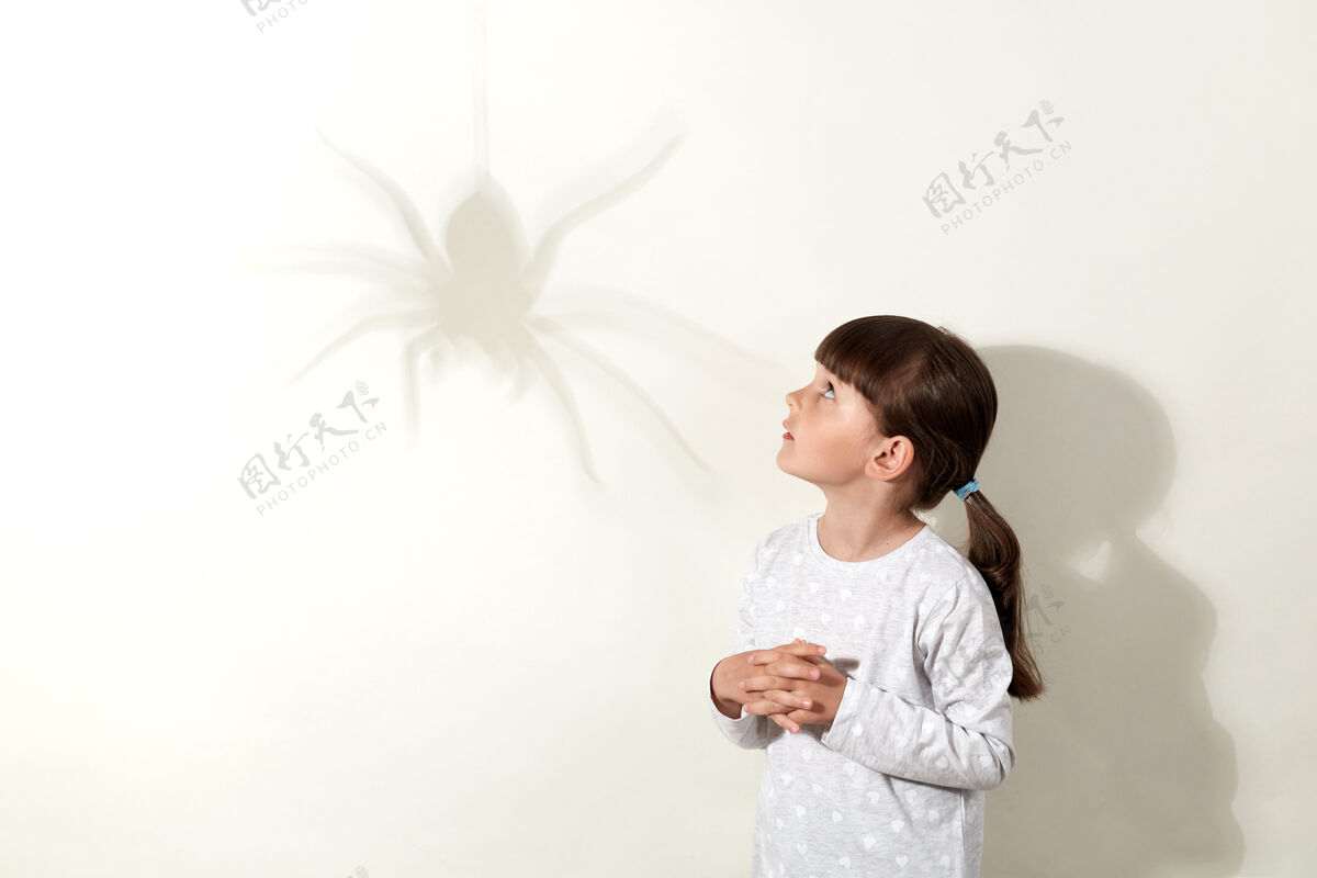 母马蜘蛛在墙上投下巨大的阴影 小女孩儿怕虫子 用害怕的眼神看着虫子 手放在胸前 穿着白衬衫 头发乌黑的精神墙幽灵