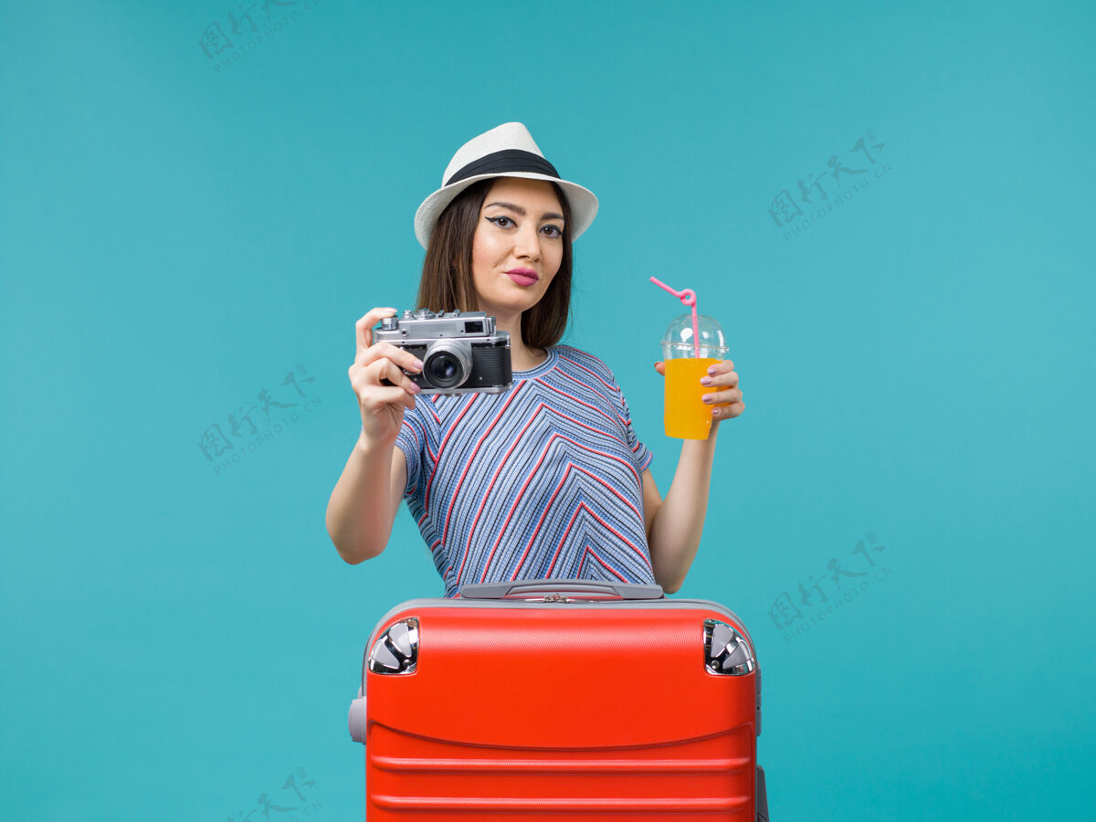 旅程正面图：度假中的女人拿着果汁和相机在蓝色的背景下航行 夏天出海美丽相机人