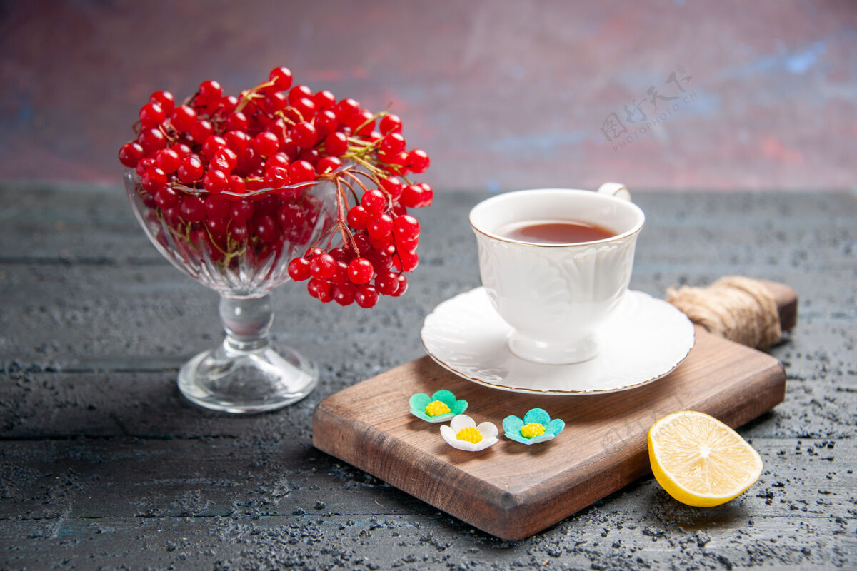 板正面图一杯红醋栗 一杯茶放在砧板上 一片柠檬放在深色的背景上茶杯子咖啡