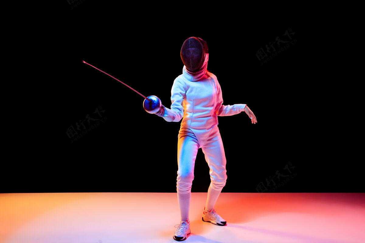 运动运动身着击剑服装的少女 手拿剑 黑色背景 霓虹灯年轻模特在运动中练习和训练 动作广告空间运动 年轻 健康的生活方式形状栅栏运动员