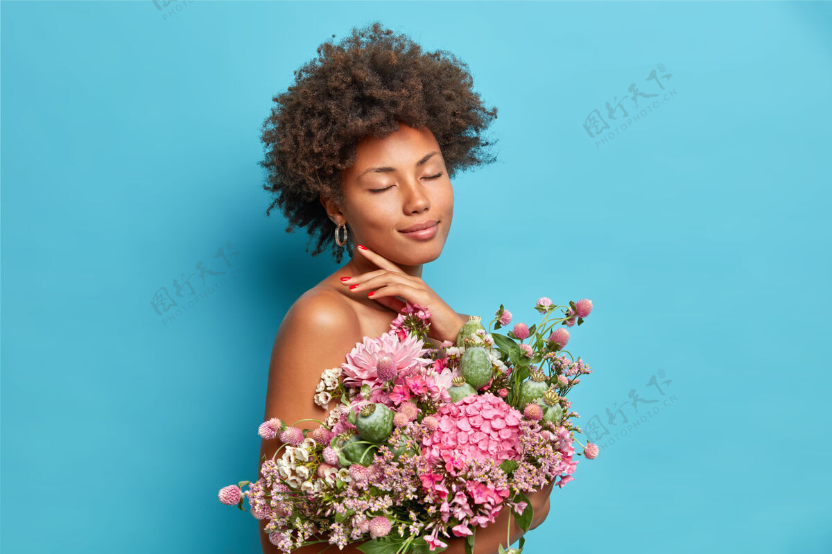 高兴快乐温柔的女模特触碰下巴线闭上眼睛享受可爱的瞬间半裸摆出一束美丽的花朵隔离在蓝色的墙上脸感性花
