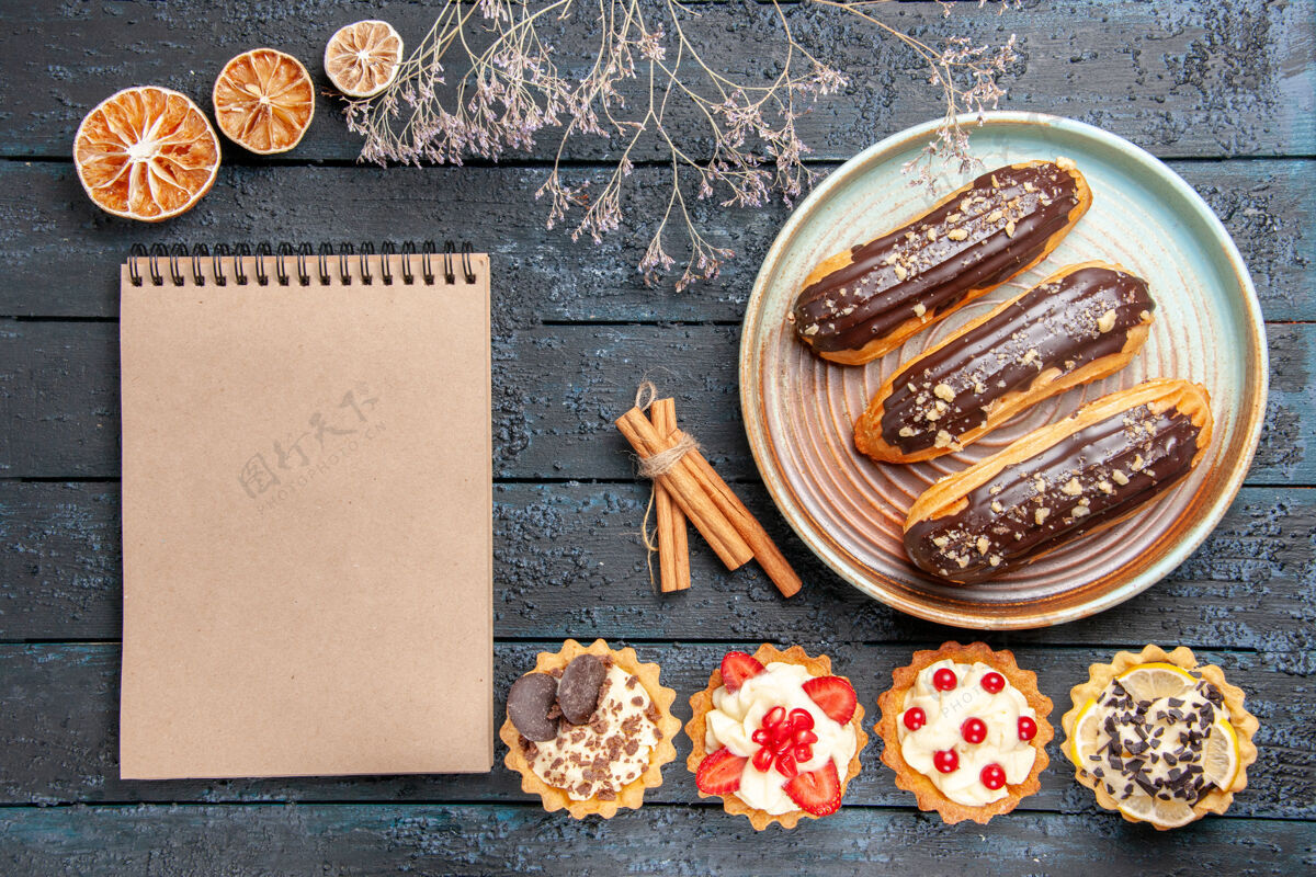 桌子俯瞰图：椭圆形盘子上的巧克力馅饼 肉桂干橘子和深色木桌上的笔记本顶部酸肉桂