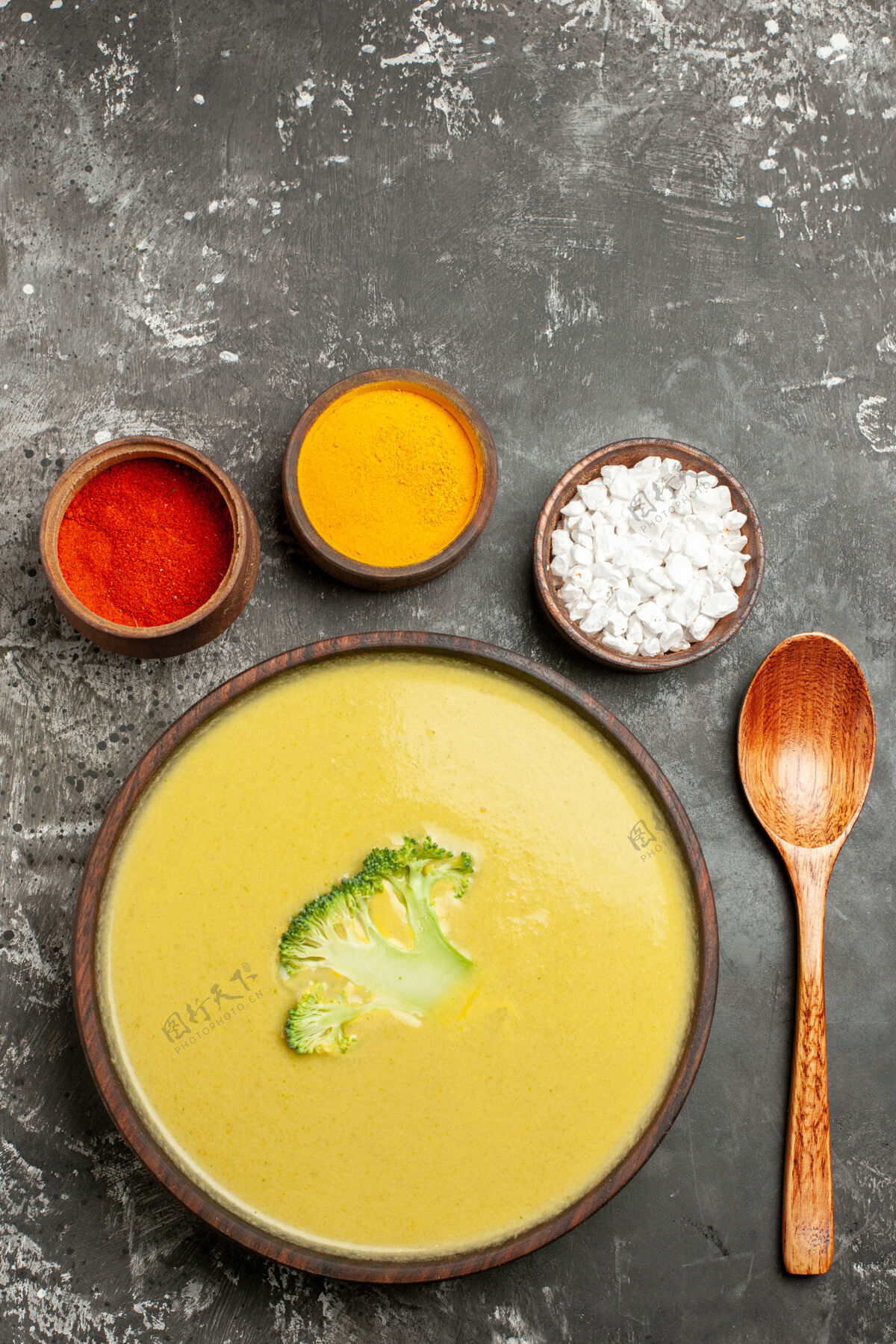 食物棕色碗里的奶油西兰花汤的垂直视图不同的香料和勺子放在灰色的桌子上晚餐美味碗