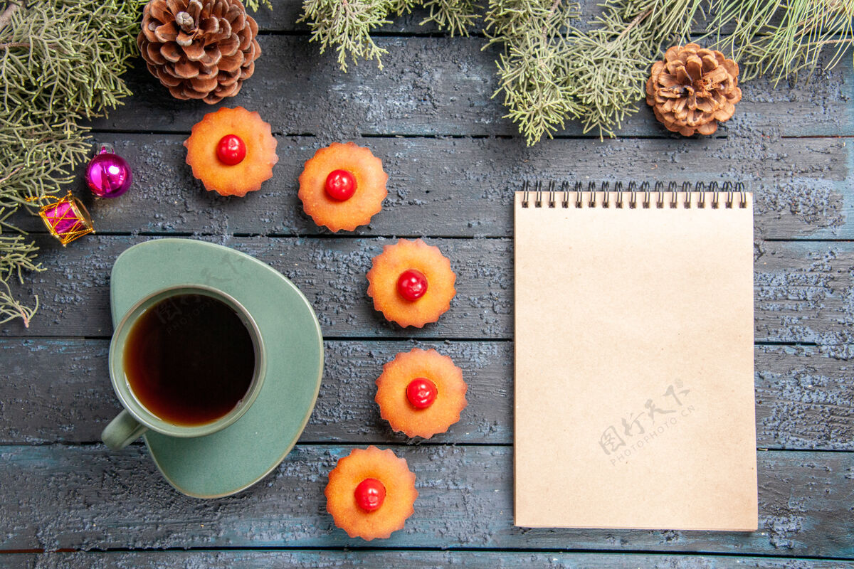 桌子俯视图圆形樱桃纸杯蛋糕杉树树枝圣诞玩具锥一杯茶一本笔记本在深色木桌上顶部咖啡深色