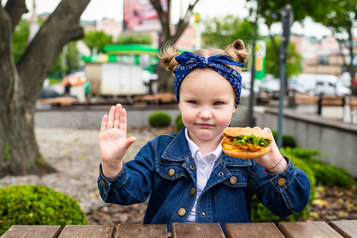 汉堡可爱的小女孩在户外咖啡厅吃东西前 手拿汉堡包 做了一个停止的手势休闲孩子小女孩