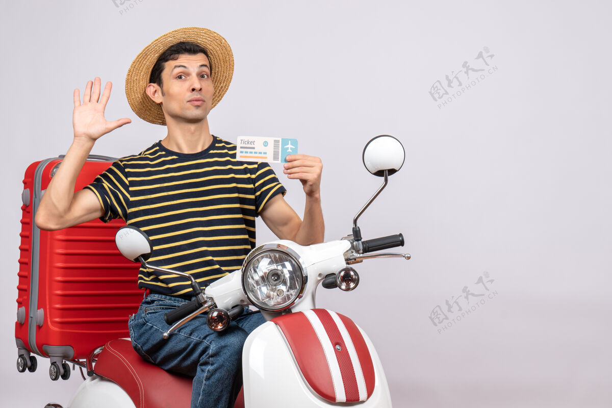 前面手持飞机票 手持轻便摩托车 头戴草帽的年轻人挥手致意的正面图输送机摩托车挥手