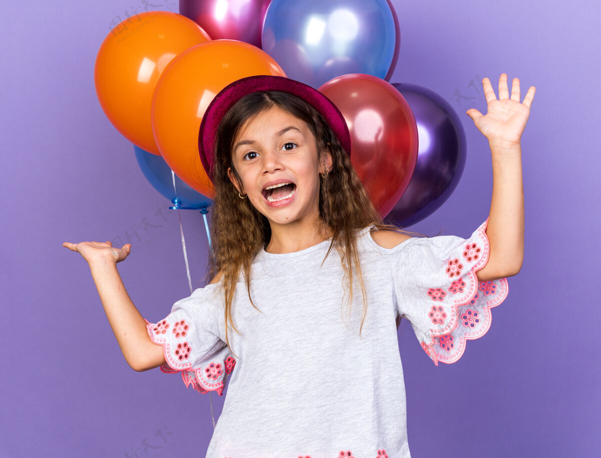 高加索快乐的小白种女孩 戴着紫色的派对帽 站在氦气球前面 氦气球被隔离在紫色的墙上 还有复制空间提高孤立前面