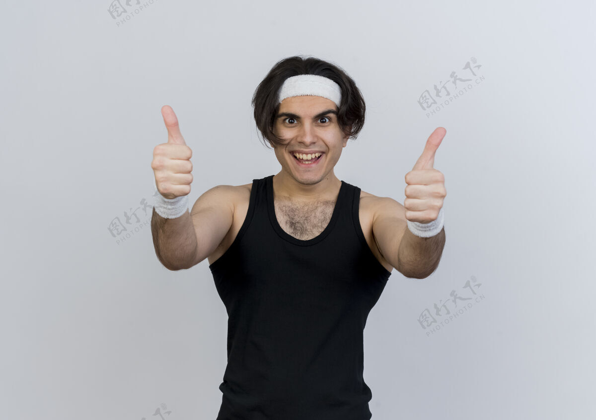 人身穿运动服 头戴头巾的年轻人站在白色的墙壁上 微笑着竖起大拇指看着前方姿势脸运动