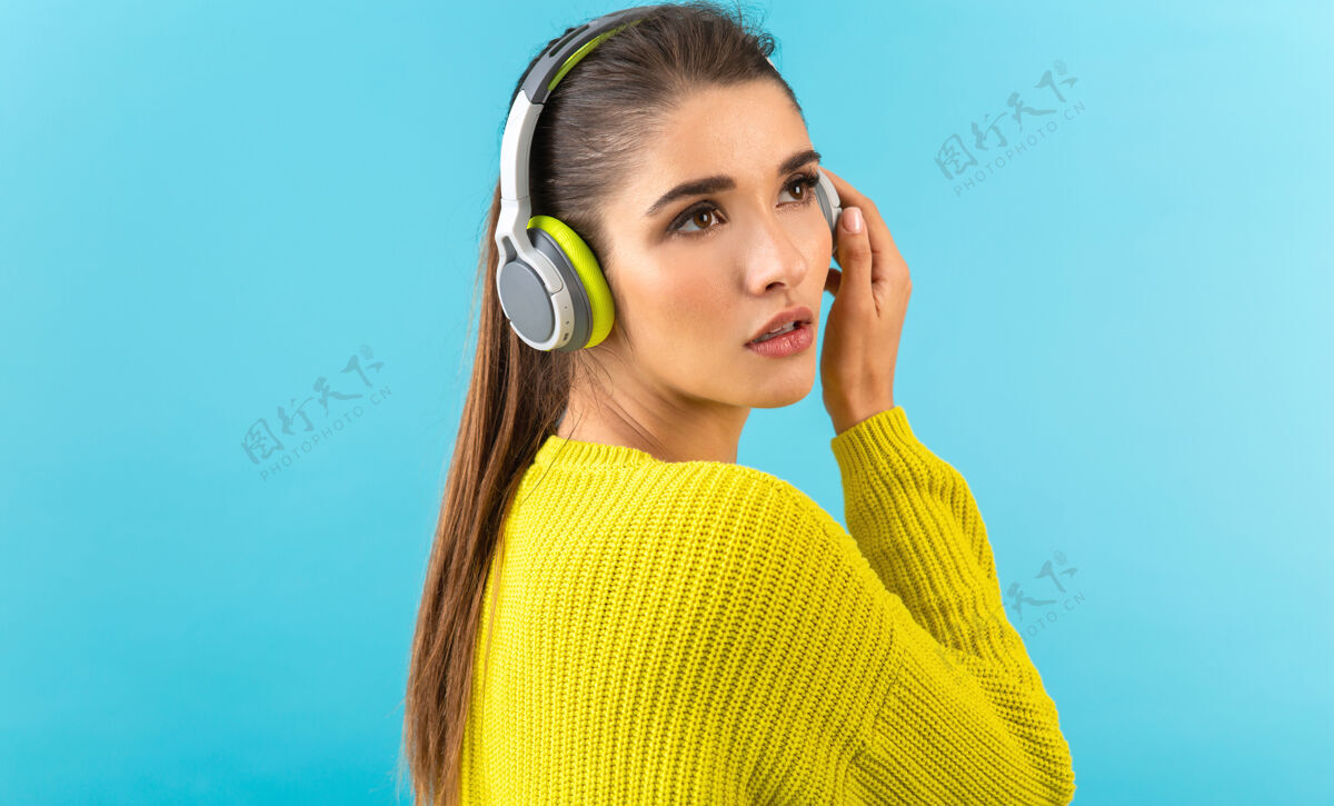 女人戴着无线耳机听音乐的女人开心地穿着黄色针织毛衣摆着蓝色的姿势无线耳机时髦