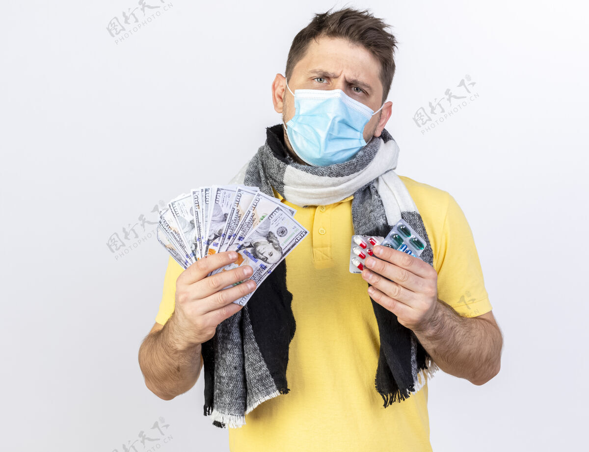 年轻人无知的年轻金发病患戴着医用面罩和围巾 手里拿着钱和几包药片 隔离在白墙上斯拉夫市民包装