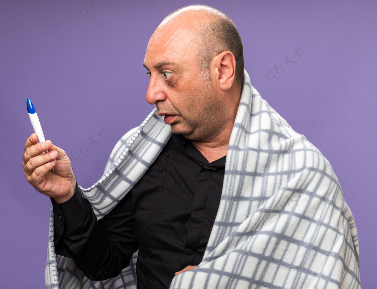 抱着震惊的成年病高加索男子包裹在格子布举行 看着温度计隔离在紫色墙上的复制空间包裹疾病成人